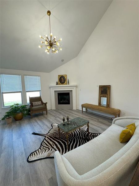 Living room featuring high vaulted ceiling, hardwood / wood-style floors, a tiled fireplace, and a chandelier