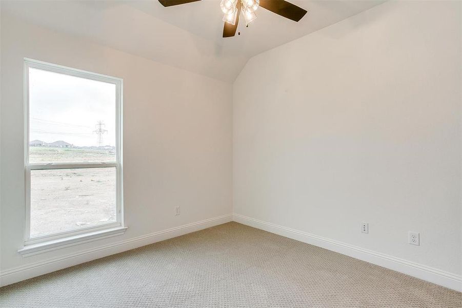 Carpeted empty room with ceiling fan, plenty of natural light, and vaulted ceiling