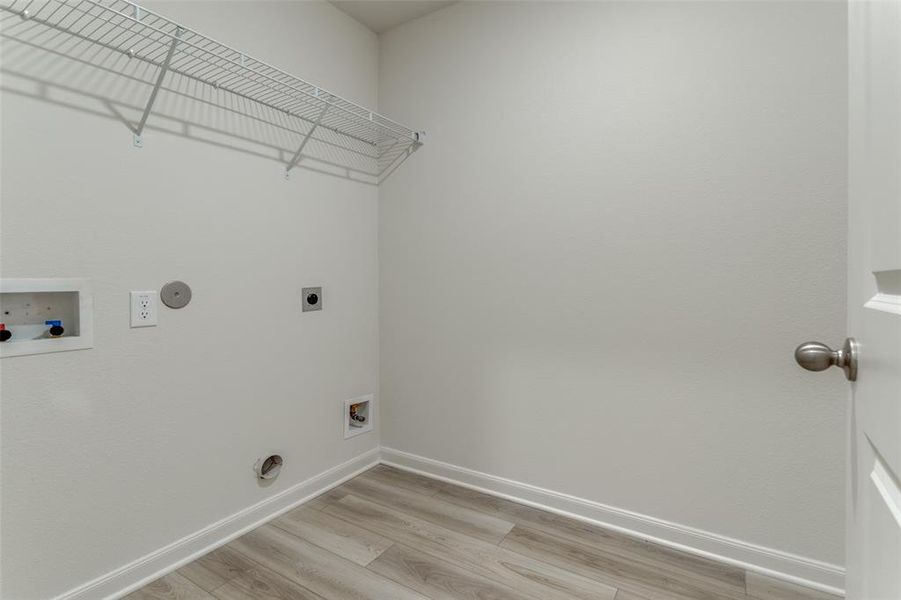 Clothes washing area featuring hookup for an electric dryer, light wood-type flooring, and washer hookup