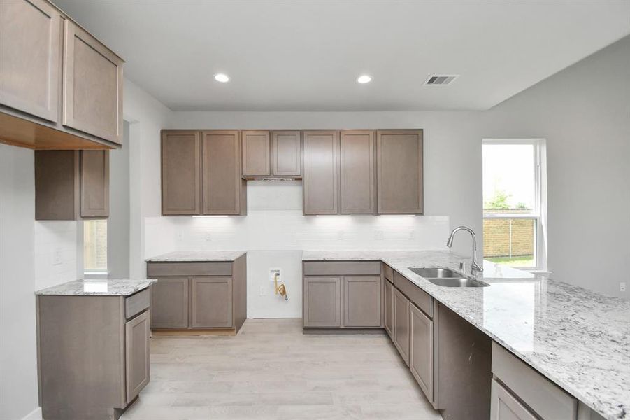 Culinary haven, featuring granite countertops, a tile backsplash, stainless steel appliances (to be installed), and 42” upper cabinets. Photo shown is example of completed home with similar plan.