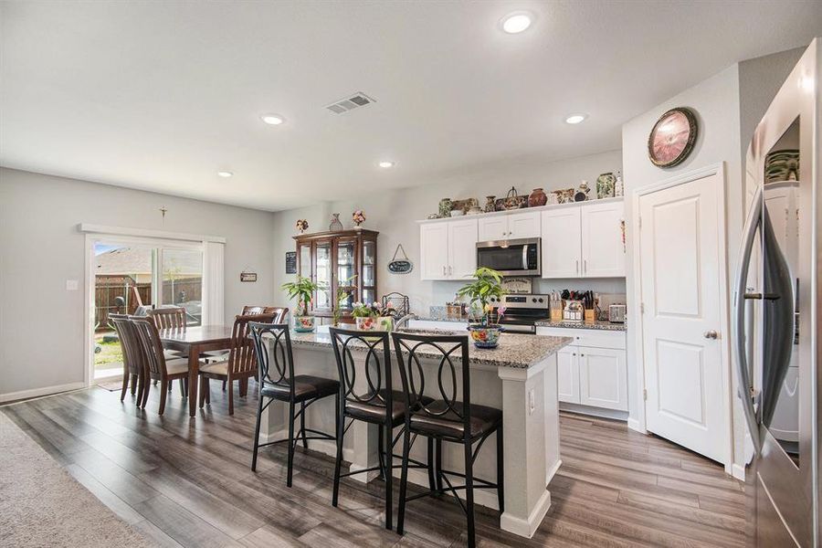 Kitchen with wood-type flooring, appliances with stainless steel finishes, white cabinets, and a kitchen island with sink