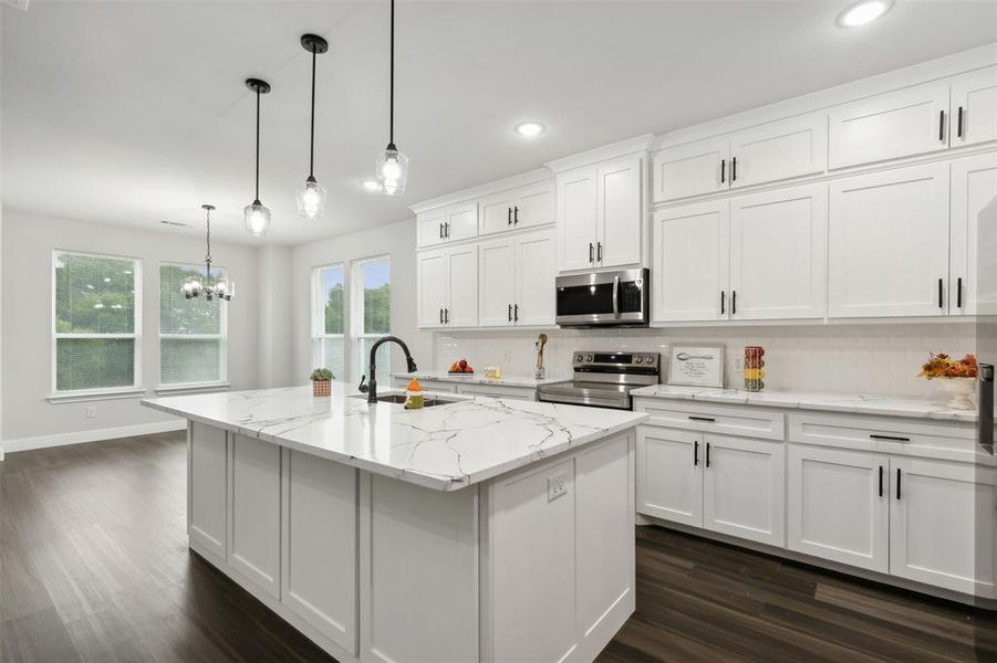 Kitchen with white cabinets, appliances with stainless steel finishes, sink, pendant lighting, and a center island with sink