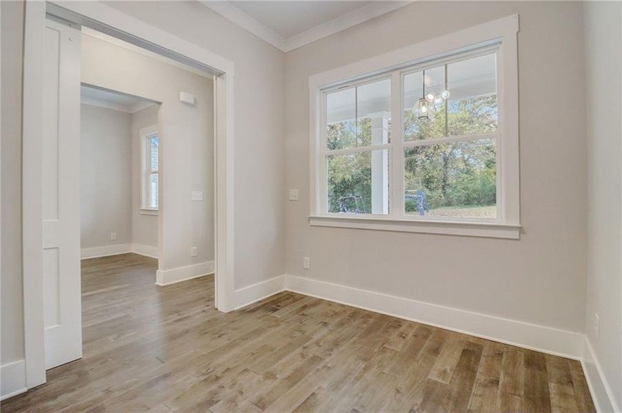 Unfurnished room featuring an inviting chandelier, light wood-type flooring, and crown molding