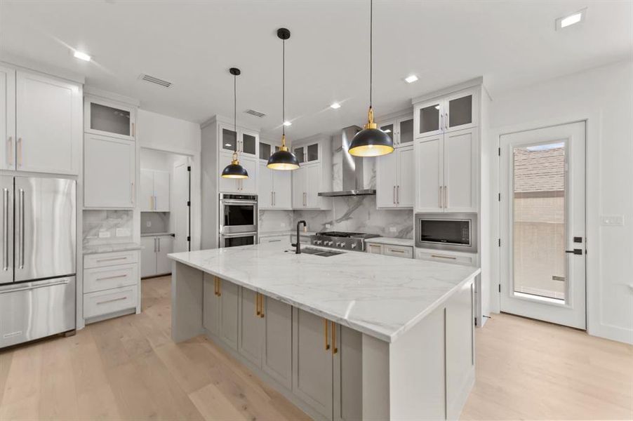 Kitchen with an island with sink, wall chimney exhaust hood, backsplash, white cabinetry, and stainless steel appliances