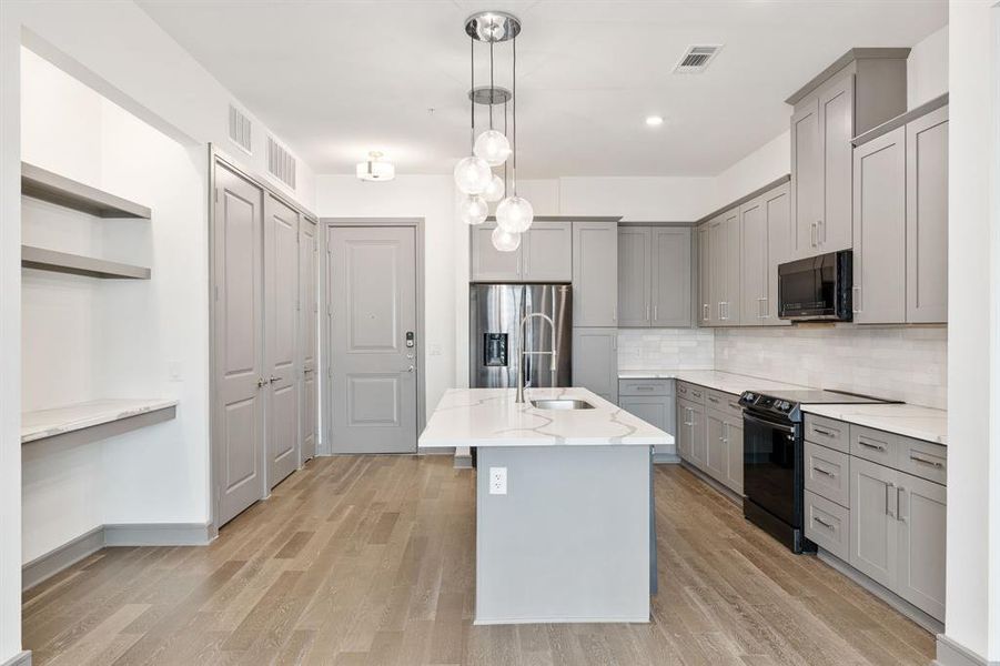 Kitchen featuring gray cabinetry, black appliances, tasteful backsplash, and light wood-type flooring