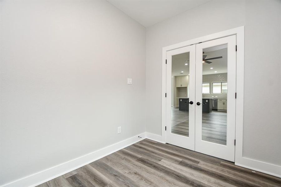 This is a great size, in home office or study room featuring neutral walls, wood-look flooring, and French doors with glass panels that lead to family room  and open kitchen.