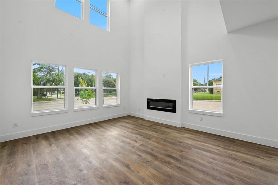 Unfurnished living room with hardwood / wood-style flooring, a healthy amount of sunlight, and a towering ceiling