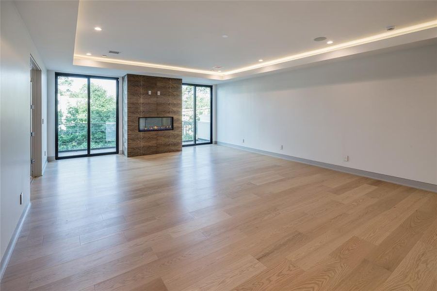 Stunning oversized primary suite with porcelain tile surrounding the fire place, seating area, wide plank wood flooring and sliding glass doors leading a private terrace