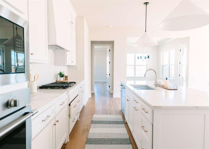 Kitchen with light hardwood / wood-style flooring, white cabinetry, sink, pendant lighting, and a kitchen island with sink