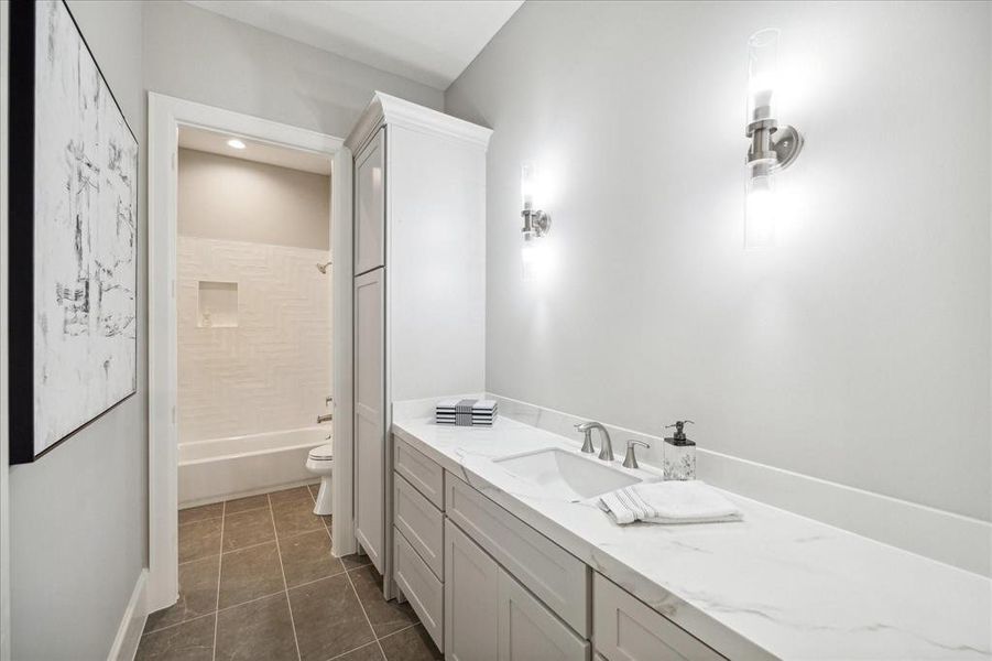 This is a modern bathroom with a double vanity, ample cabinet space, and sleek fixtures. It features a shower/tub combo and is accented by stylish wall art and elegant lighting.