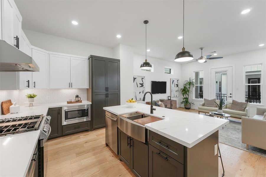 Chefs open kitchen and living space features stainless steel appliances, a modern island with a sink, quartz countertops, and custom black matte pendant lighting.