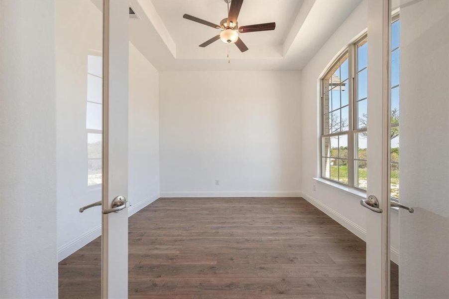 Empty room with french doors, dark hardwood / wood-style floors, ceiling fan, and a raised ceiling