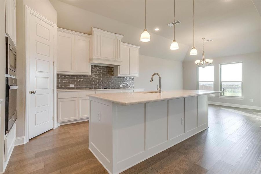 Kitchen with a chandelier, white cabinets, hanging light fixtures, stainless steel appliances, and a center island with sink