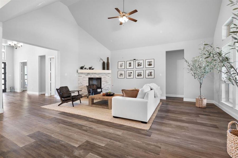 Living room featuring a stone fireplace with gas, wood-style floors, ceiling fan, and high vaulted ceiling