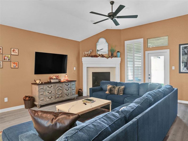 Spacious living room with gas fireplace and plantation shutters leading to a covered patio and backyard.