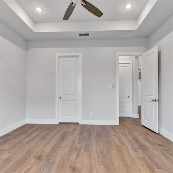 Unfurnished bedroom featuring a tray ceiling, light hardwood / wood-style flooring, and ceiling fan