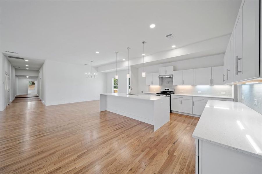 Kitchen featuring light hardwood / wood-style flooring, white cabinets, sink, pendant lighting, and an island with sink