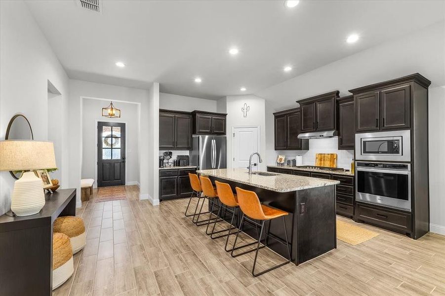 Kitchen featuring sink, an island with sink, light hardwood / wood-style floors, a kitchen bar, and stainless steel appliances