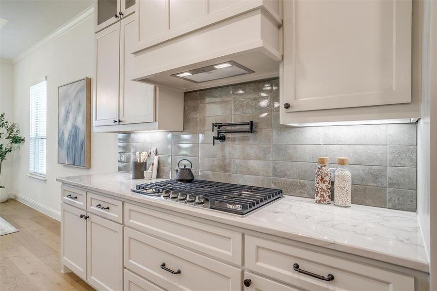 Kitchen featuring decorative backsplash, crown molding, light wood-type flooring, stainless steel gas stovetop, and white cabinetry