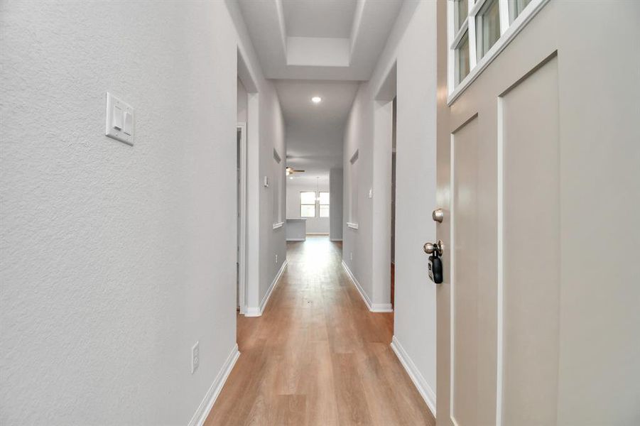 Step into this bright and welcoming entryway with light hardwood floors, tray ceiling, and recessed lighting, offering a modern and spacious feel as you step inside.