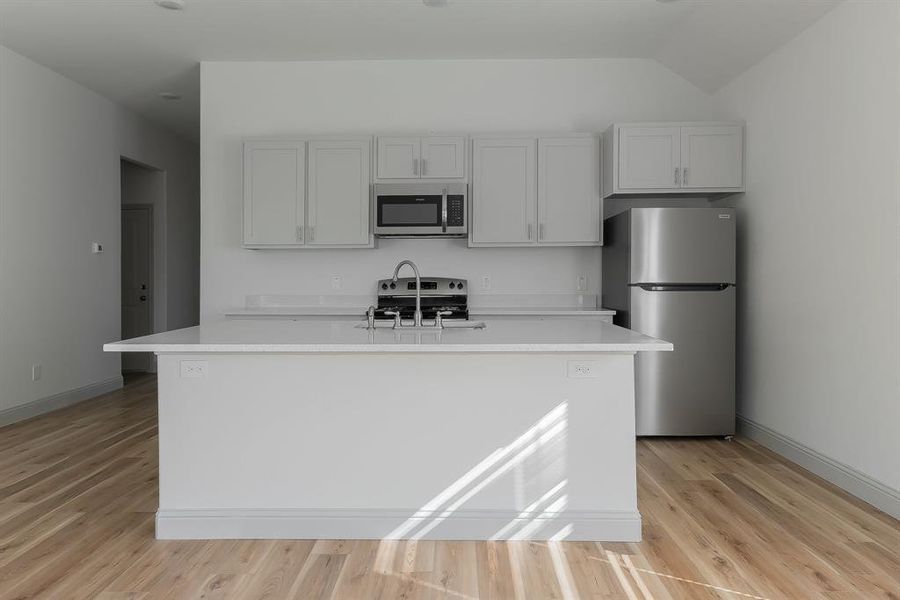 Kitchen featuring an island with sink, sink, appliances with stainless steel finishes, light wood-type flooring, and vaulted ceiling