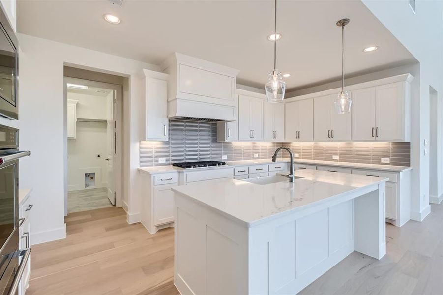 Kitchen featuring white cabinets, tasteful backsplash, a kitchen island with sink, pendant lighting, and sink