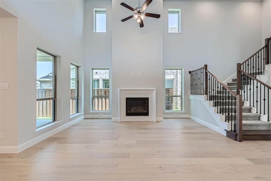 Unfurnished living room featuring a high ceiling, ceiling fan, and light hardwood / wood-style floors