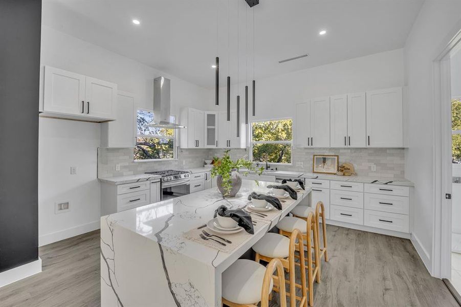 Kitchen with stainless steel range with gas stovetop, white cabinets, a kitchen island, and island range hood