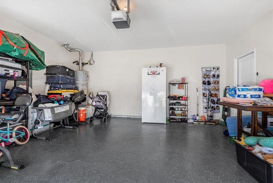 Garage with white refrigerator, a garage door opener, and strapped water heater