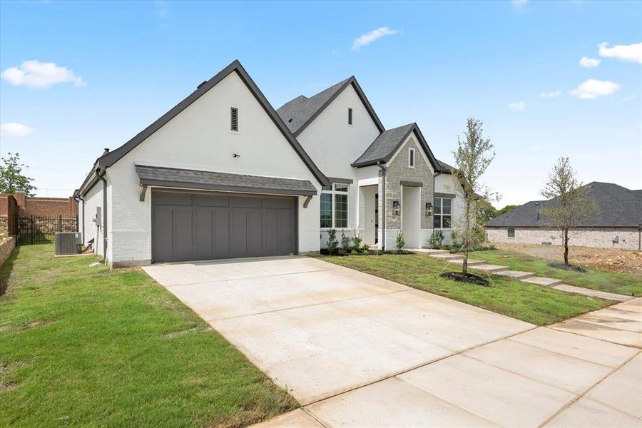 French provincial home featuring a garage, central AC unit, and a front yard