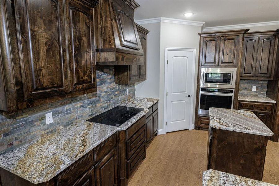 Kitchen with light hardwood / wood-style floors, a center island, stainless steel appliances, dark brown cabinetry, and light stone countertops