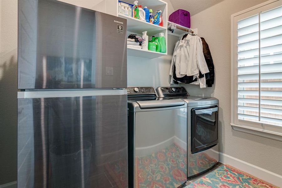 Clothes washing area featuring separate washer, dryer and room for refrigerator.