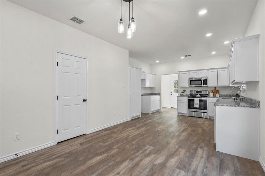 Kitchen featuring appliances with stainless steel finishes, white cabinetry, dark wood-type flooring, and pendant lighting