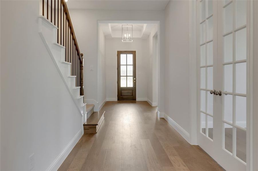 Foyer with light hardwood / wood-style floors, a notable chandelier, french doors, and a tray ceiling