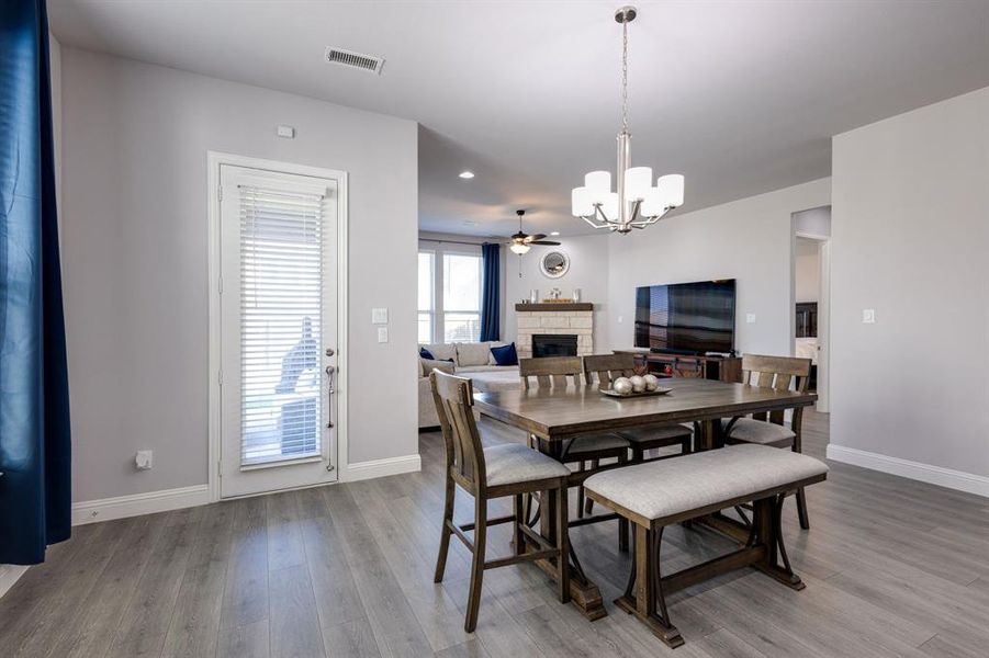 Dining area featuring wood-type flooring, a stone fireplace, and ceiling fan with notable chandelier