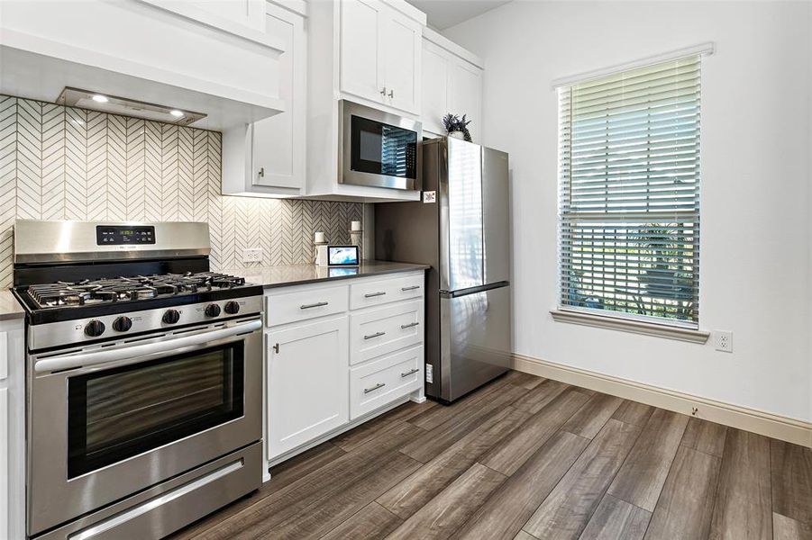 Kitchen with backsplash, stainless steel appliances, dark wood-type flooring, custom range hood, and white cabinets