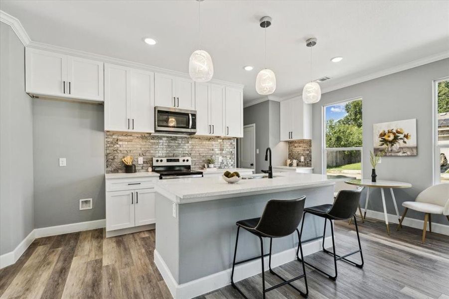 Kitchen featuring white cabinetry, pendant lighting, stainless steel appliances, crown molding, and a kitchen island with sink