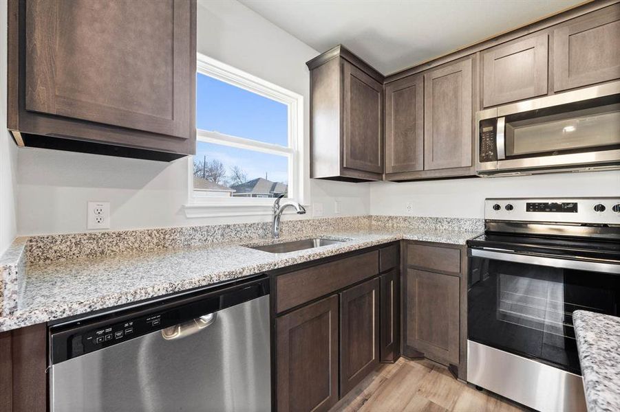 Kitchen featuring light hardwood / wood-style flooring, light stone countertops, stainless steel appliances, sink, and dark brown cabinets