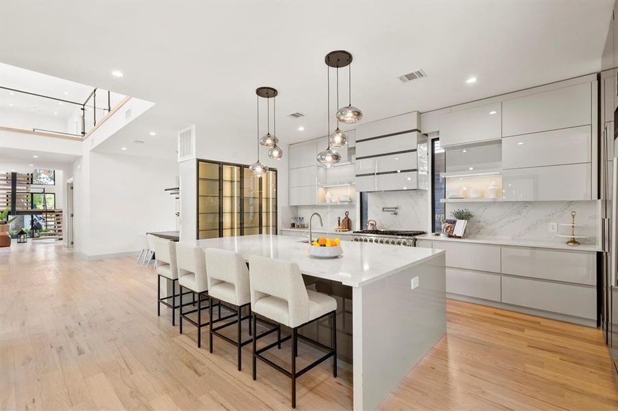 Kitchen featuring hanging light fixtures, a large island, light hardwood / wood-style flooring, white cabinetry, and decorative backsplash