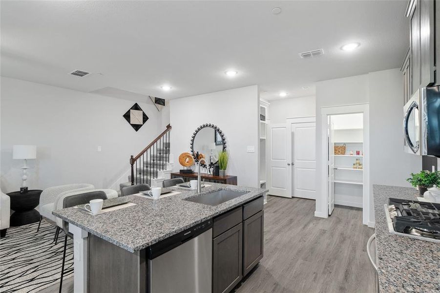 Kitchen featuring light stone countertops, a center island with sink, light hardwood / wood-style floors, stainless steel appliances, and sink