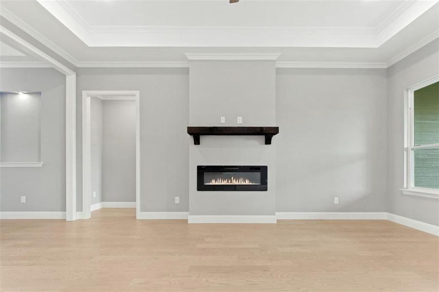 Unfurnished living room featuring light wood-type flooring, a raised ceiling, and crown molding