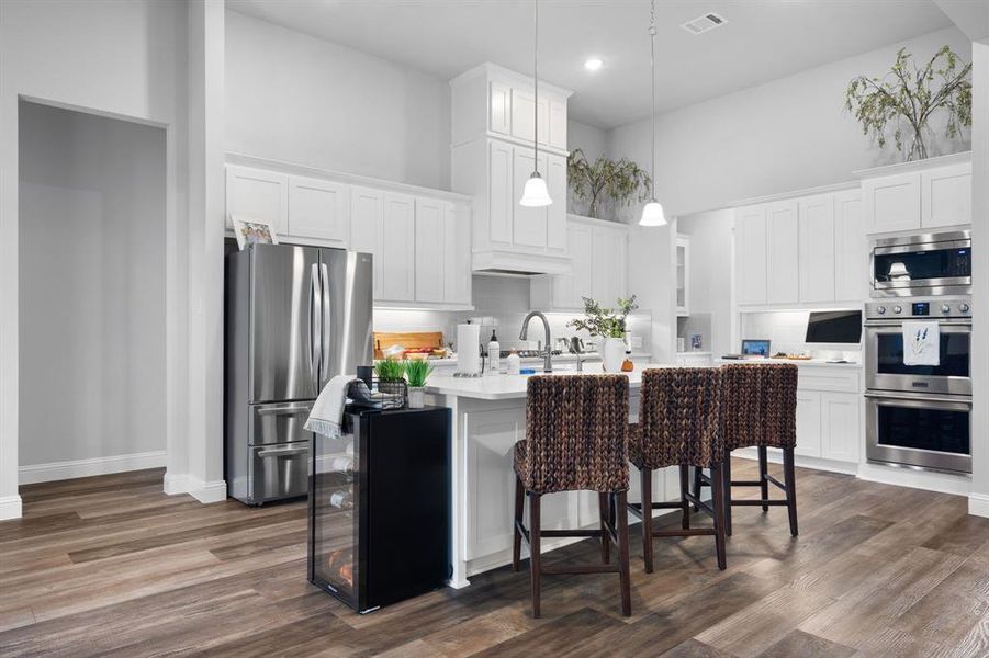 Kitchen has stainless steel appliances, a towering ceiling, and white cabinetry