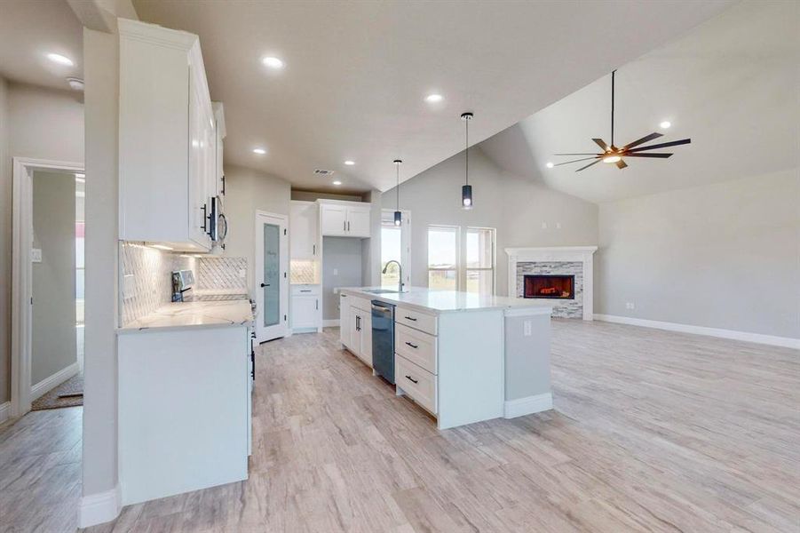 Kitchen with white cabinetry, an island with sink, a stone fireplace, ceiling fan, and sink