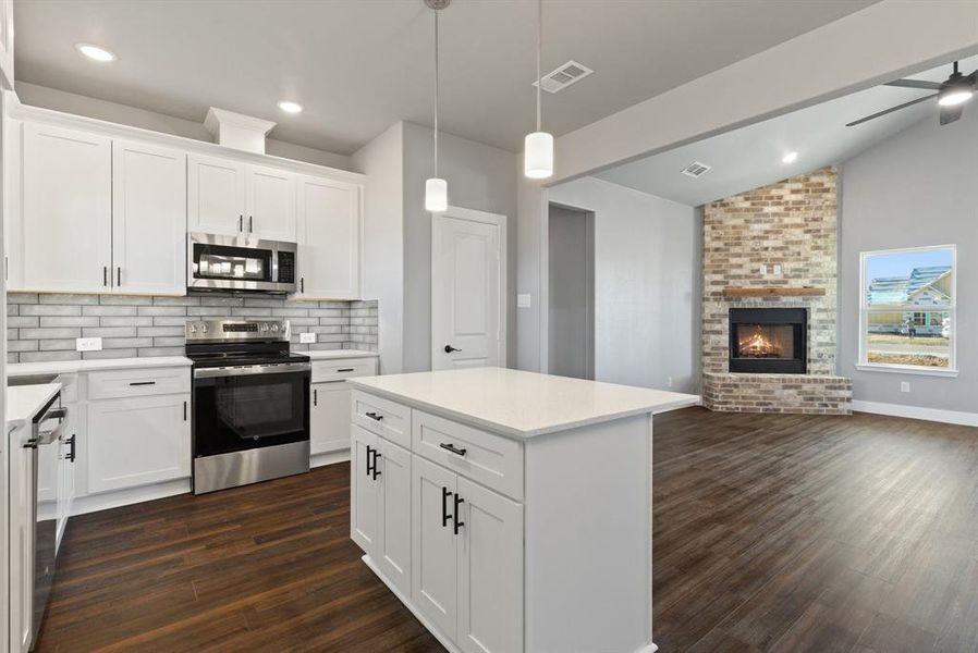 Kitchen featuring appliances with stainless steel finishes, dark hardwood / wood-style flooring, a brick fireplace, pendant lighting, and white cabinetry