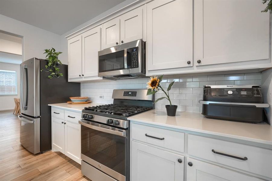 Kitchen with tasteful backsplash, appliances with stainless steel finishes, light hardwood / wood-style floors, and white cabinets