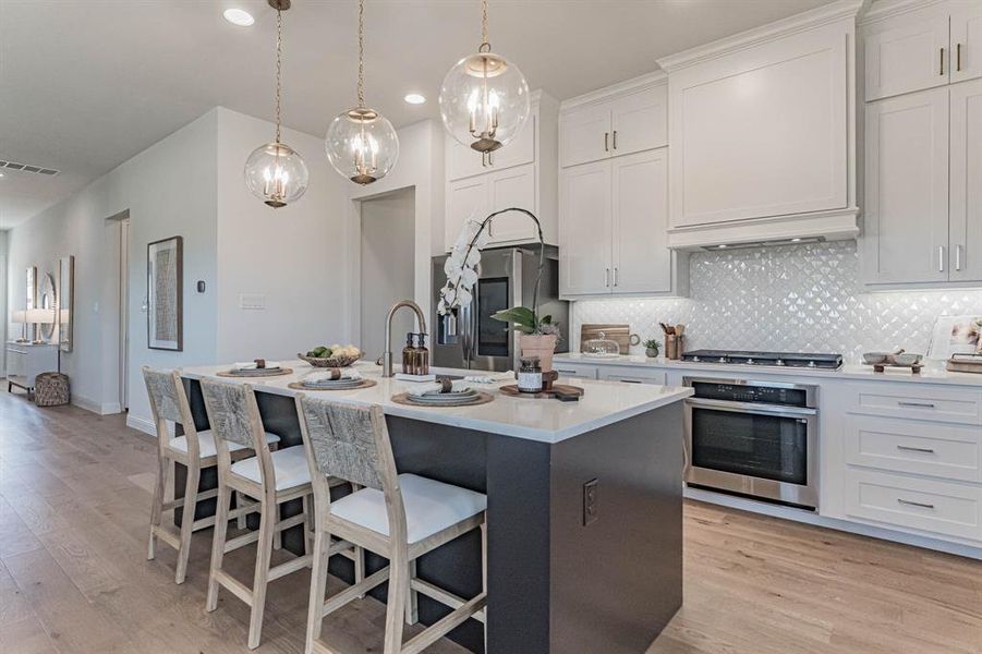 Kitchen featuring tasteful backsplash, light wood-type flooring, white cabinets, a kitchen island with sink, and appliances with stainless steel finishes