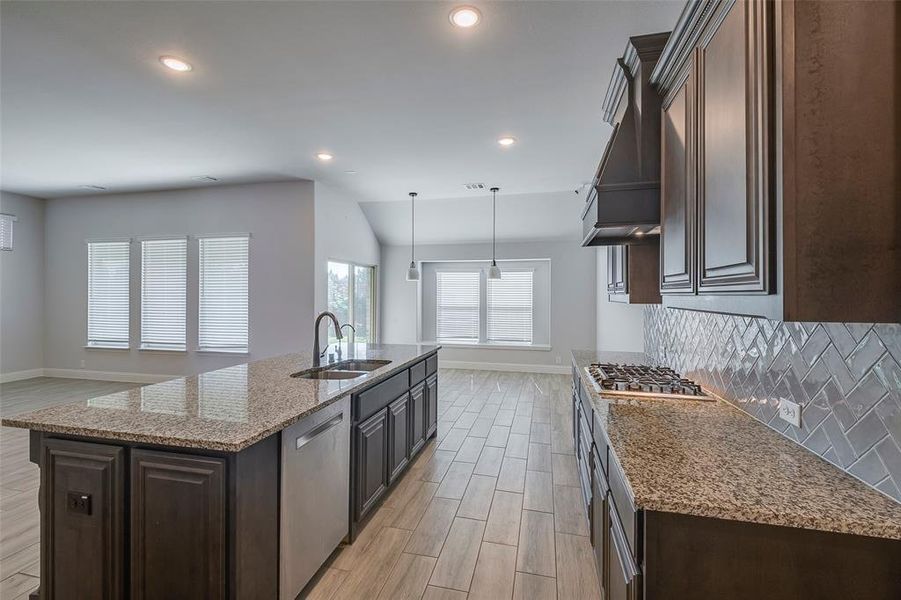 Kitchen with tasteful backsplash, appliances with stainless steel finishes, sink, light hardwood / wood-style flooring, and a center island with sink