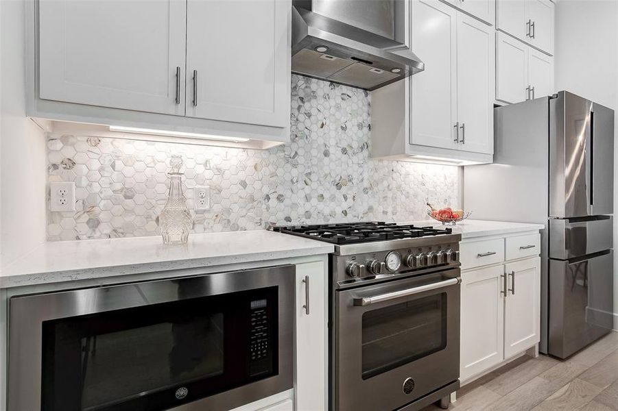 Kitchen with light wood-type flooring, high end stove, black microwave, backsplash, and wall chimney range hood