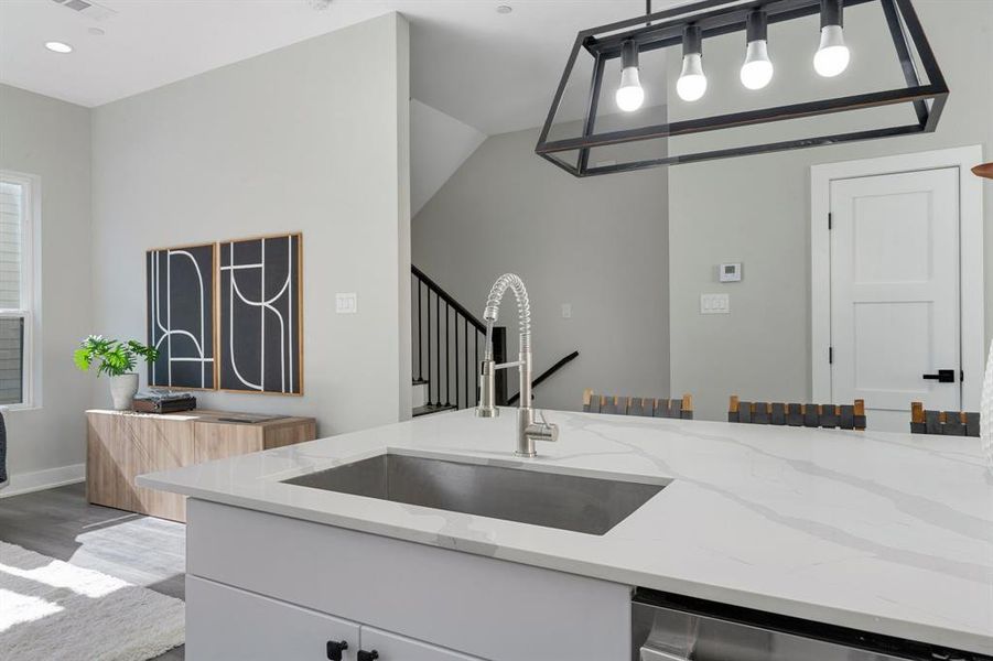 Kitchen with hanging light fixtures, light stone counters, sink, and light wood-type flooring