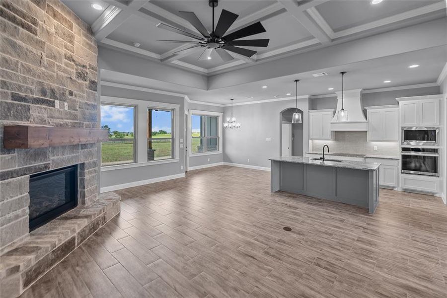 Kitchen with appliances with stainless steel finishes, a center island with sink, ceiling fan with notable chandelier, custom exhaust hood, and coffered ceiling